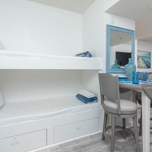 This cozy nook features a bunk bed, a dining area with blue accents, and a view of the beach through large sliding doors