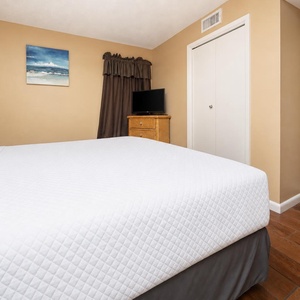 Master suite bedroom featuring a king bed, a flat-screen TV, and warm tones, perfect for relaxation after a day at the beach