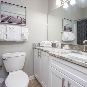 Bright guest bathroom featuring a sleek countertop, neatly arranged towels, and a tub/shower combo with a stylish curtain