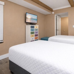 Guest bedroom featuring two cozy full beds, a colorful dresser, and a wall-mounted TV for entertainment