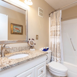 The bathroom features a granite countertop, decorative mirror, and nautical-themed shower curtain for a refreshing experience