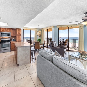 The open living area features a modern kitchen with wood cabinetry, a breakfast bar, and a stunning beachfront view