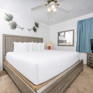 Bright and airy bedroom featuring a king bed, decorative palm accents, a cozy lamp, and a TV for entertainment
