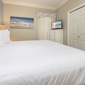 The bedroom featuring a large king bed, a TV on a dresser, and coastal artwork enhancing the serene atmosphere