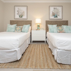 Inviting guest room featuring two queens, decorative pillows, and a cozy area rug