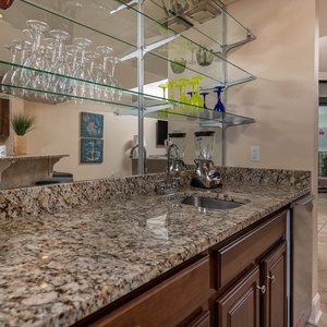 This stylish wet bar features a granite countertop, glassware display, and a cozy seating area for relaxation
