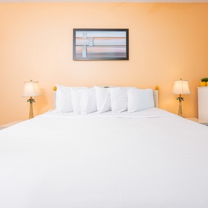 The master bedroom features a large king bed with multiple pillows, warm peach walls, and stylish bedside lamps