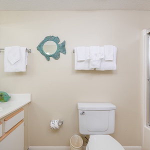 Bright guest bathroom featuring a playful fish mirror, fresh towels, and a tub/shower combo for a refreshing retreat