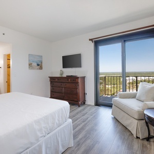 Master bedroom featuring a cozy king bed, flat-screen TV, and a balcony with a beautiful view of the landscape