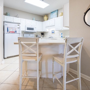 Bright white cabinetry complements the breakfast bar with stools, creating a welcoming space in this fully-equipped kitchen
