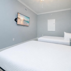 Relaxing guest room featuring two queens, a wall-mounted TV, and cheerful decor for a comfortable stay