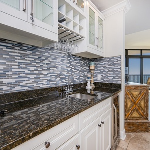 Stylish kitchen wet bar featuring sleek granite countertops, wine cooler, blender, and stunning balcony view