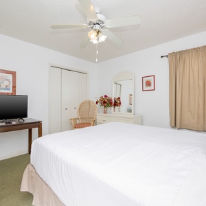 This guest bedroom features a queen bed, a TV on a wooden table, and a cozy chair beside a dresser with decorative accents