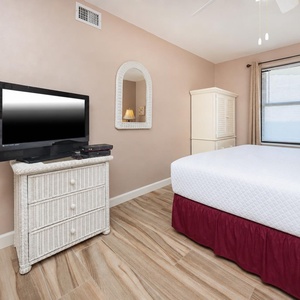 Guest room featuring a queen bed, a flat-screen TV on a wicker dresser, and a cozy atmosphere