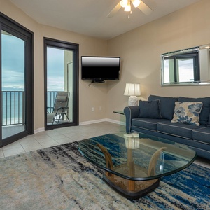 Cozy living area features a blue sofa with queen sleeper, glass coffee table, and stunning views of the beach