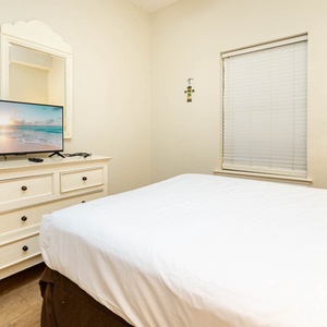 Cozy guest bedroom featuring a queen bed, a TV for entertainment, and soft natural light from the window