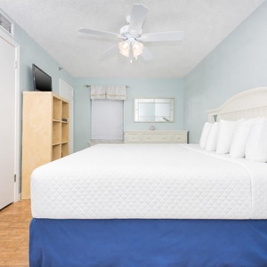Soothing guest bedroom featuring a king bed with white linens, a dresser, and a mounted TV