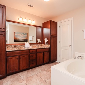 The master bath features elegant dark wood cabinetry, a spacious vanity with granite countertops, and a relaxing jetted tub