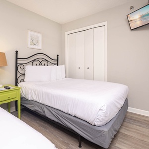 A cozy guest bedroom features two double beds, a vibrant green nightstand with a lamp, and a TV for entertainment