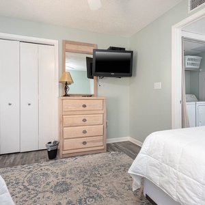 Bright guest bedroom featuring twin beds, a dresser with a TV, showing the laundry area behind a curtain for convenience