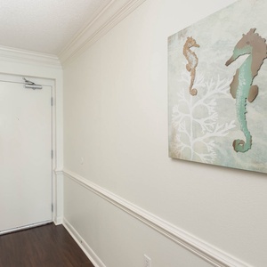 Welcoming entryway featuring a white door, dark wood flooring, and seahorse-themed artwork on a light wall