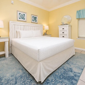 Bright yellow walls complement the cozy king bed, with a bedside lamp and a dresser enhancing the inviting atmosphere