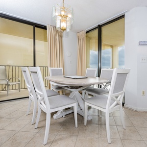 Bright dining area featuring a round table with six chairs, accented by a stylish chandelier and views of the beachfront