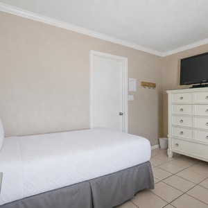 Cozy guest bedroom features two twin beds, a dresser, and a mounted TV against a soft beige wall
