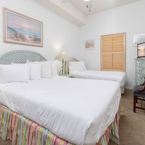 Brightly decorated guest bedroom features two double beds with colorful skirts, TV, and coastal art, creating a relaxed vibe