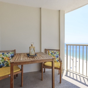 This balcony features a cozy wooden table and chairs with colorful cushions, offering a stunning beachfront view