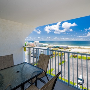 Enjoy a relaxing beach view from the balcony, featuring a glass-top table and comfortable seating for your morning coffee