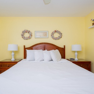 The bedroom features a cheerful yellow wall, a comfortable bed with white linens, and beach-themed décor