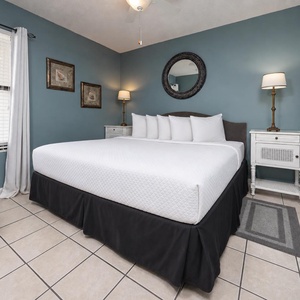 This cozy bedroom features a large bed with crisp white linens, a stylish lamp, and charming artwork on soft blue walls