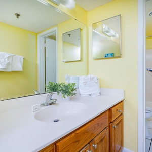 Bright master bath featuring a light yellow wall, wooden cabinetry, and a shower with a blue curtain for a cheerful ambiance