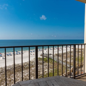 The balcony offers a captivating view of the beach, featuring colorful umbrellas and soft white sand beneath a clear blue sky