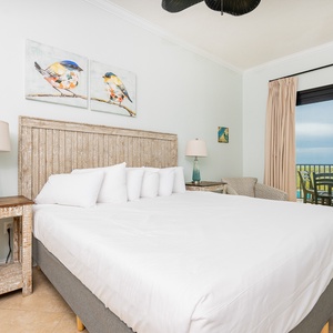 Decorated master bedroom features a king bed, stylish nightstand with a lamp, and access to a balcony with beach views