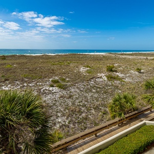 Poolside seating surrounds a tranquil pool area with a gazebo, leading to a scenic view of the beach and Gulf beyond