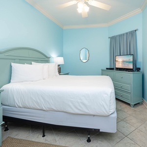 Rest in this serene guest bedroom featuring a plush queen bed, soft blue walls, and a TV for your entertainment