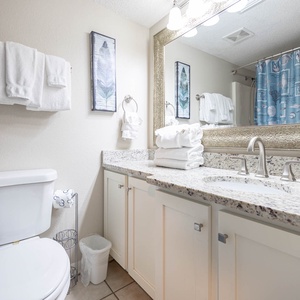Bright guest bathroom featuring a vanity with granite countertops, decorative blue shower curtain, and neatly stacked towels