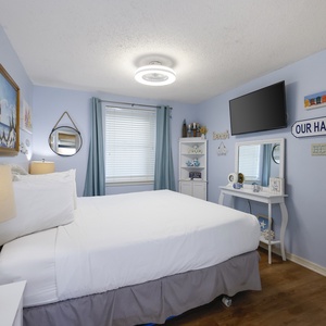 This cozy bedroom features a comfortable bed, a mounted TV, and cheerful beach-themed decor, creating a relaxing retreat