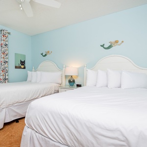 Bright guest bedroom featuring two double beds, whimsical mermaid decor, and a soothing blue color palette