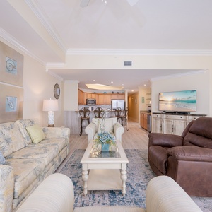 Living area featuring a cozy floral sofa, plush recliner, and a view of the modern kitchen and breakfast bar