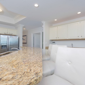Kitchen featuring sleek stainless appliances and a spacious granite countertop with stylish white bar stools