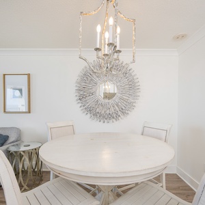 Dining area features a round white table surrounded by stylish chairs, complemented by a decorative mirror and chandelier