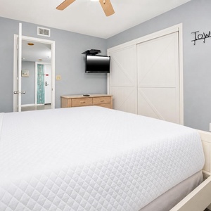 This cozy bedroom features a comfortable queen bed, bunks, a wall-mounted TV, and easy access to an adjoining bathroom