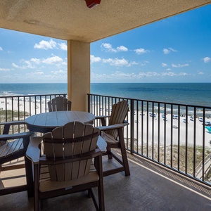 A cozy balcony features a round table and Adirondack chairs, offering a serene view of the beach and gentle waves