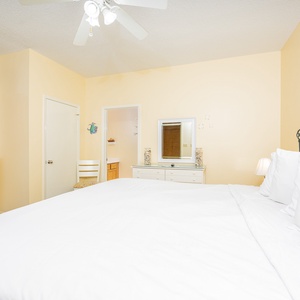 This bright guest bedroom features a king bed with crisp white linens, a colorful dresser, and a cozy chair for relaxation