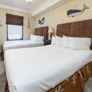 This guest bedroom features two double beds with textured headboards, a TV, and nautical decor, creating a relaxed beach vibe