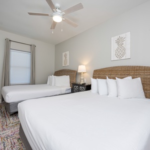 Guest bedroom featuring two queen beds with woven headboards, a stylish lamp, and cheerful pineapple wall decor