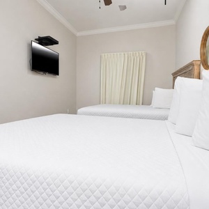 Inviting guest bedroom featuring two comfortable queen beds, a mounted TV, and soft natural light from the window
